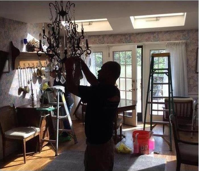 Man cleaning chandelier after damage by fire in the home